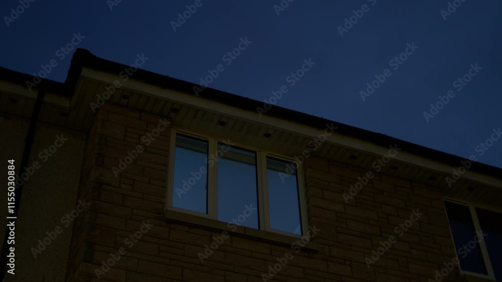Nighttime view of a house with a dark blue sky and soft moonlight in windows Nighttime view of a house with a dark blue sky and soft moonlight in windows