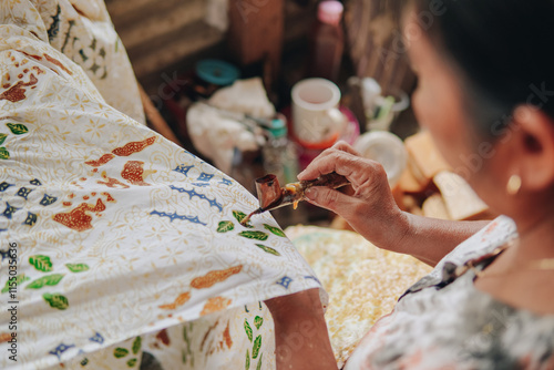 Person's hand is tracing design the pattern of batik tulis cloth using Canting.