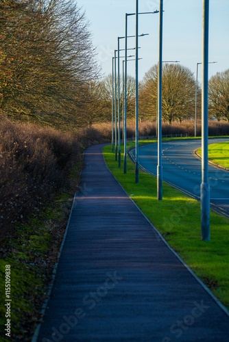 The Modern streetlights line curved pathway and road near Stansted Airport business park. Winter sunlight illuminates asphalt footpath with well-maintained grass verges and bare trees photo