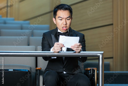 A man in a tuxedo sits in an auditorium holding script photo