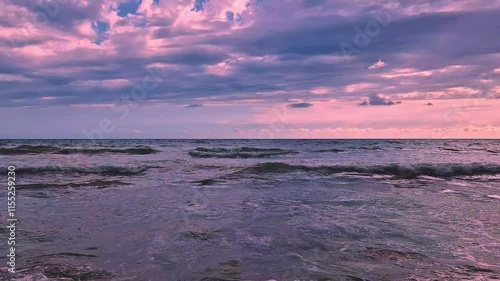 Foaming Waves Roll on a the Beach in the Ocean and a Pink Lillac Sunset Sky, Sun and Cumulus Clouds in the Sun Rays Slow Motion. Beautiful Sunset Sea Colorful Skyscraper and Clouds Background.