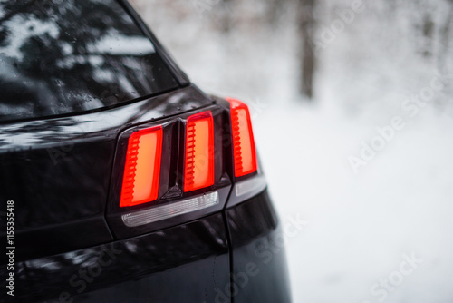 Tail light of black modern car. Rear right corner of stylish SUV or hatchback in winter forest. Three red glowing light bars in tail lights. photo