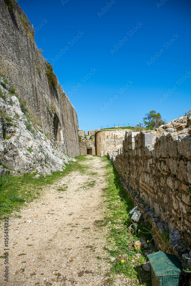 Pathway between old stone walls under blue sky Pathway between old stone walls under blue sky