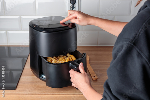 Woman at home using trendy kitchen gadget, deep fryer, selecting program on small convection oven on countertop for deep frying without oil, healthy way to cook fried food photo