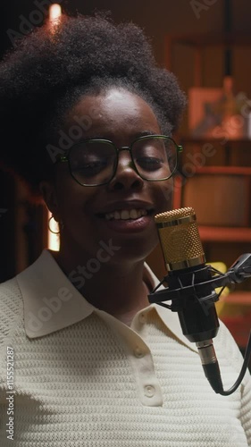 Vertical chest up shot of cheerful young African American woman speaking in microphone and starting podcast in modern broadcasting studio with neon ambient lighting creating cozy atmosphere photo