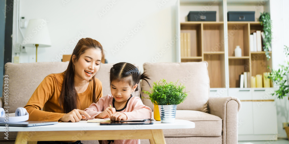 An Asian mother and her adorable daughter sit on the sofa in their living room, enjoying online learning on a tablet and reading books. A joyful family moment focused on education An Asian mother and her adorable daughter sit on the sofa in their living room, enjoying online learning on a tablet and reading books. A joyful family moment focused on education