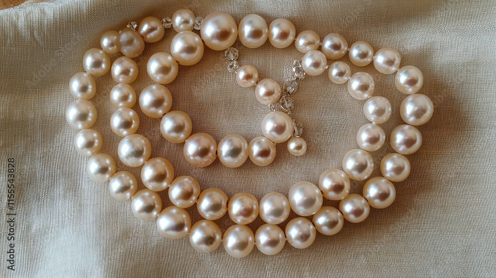 A collection of round freshwater pearls in varying sizes, arranged artistically on a satin fabric.