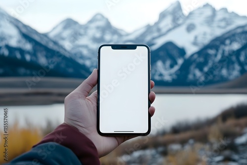 A close-up photograph of a smartphone with a white screen in the hand of someone, with the focus on the phone and hand, and a blurred mountain background photo