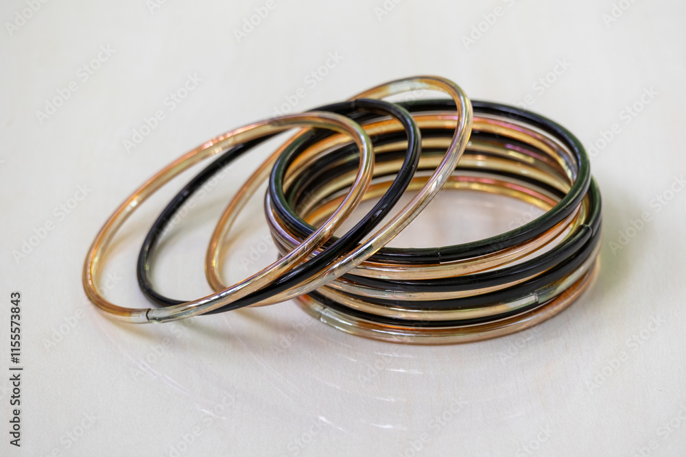 Shiny black and gold glass bangles, isolated on a wooden tile background. Churis or bangles are traditional beauty accessories worn by Asian women. Shiny black and gold glass bangles, isolated on a wooden tile background. Churis or bangles are traditional beauty accessories worn by Asian women.