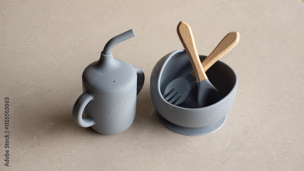 Silicone baby tableware set in gray, the first soft cup for toddlers. Baby eating utensils. Nutrition and feeding concept Silicone baby tableware set in gray, the first soft cup for toddlers. Baby eating utensils. Nutrition and feeding concept