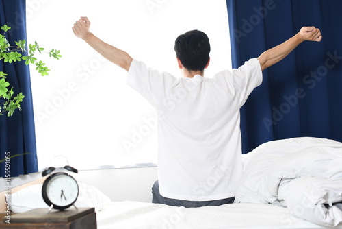 ベッドで起床後に体を伸ばす若い男性の後ろ姿