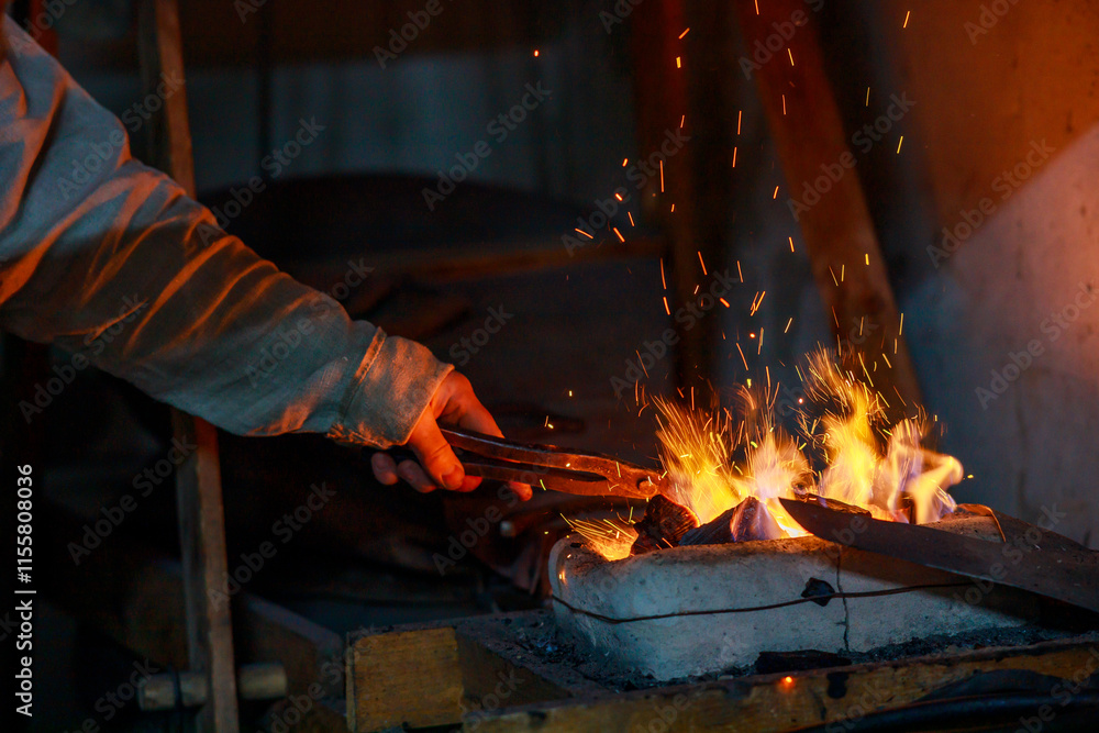 A blacksmith holds a billet in a pair of tongs over the stove A blacksmith holds a billet in a pair of tongs over the stove