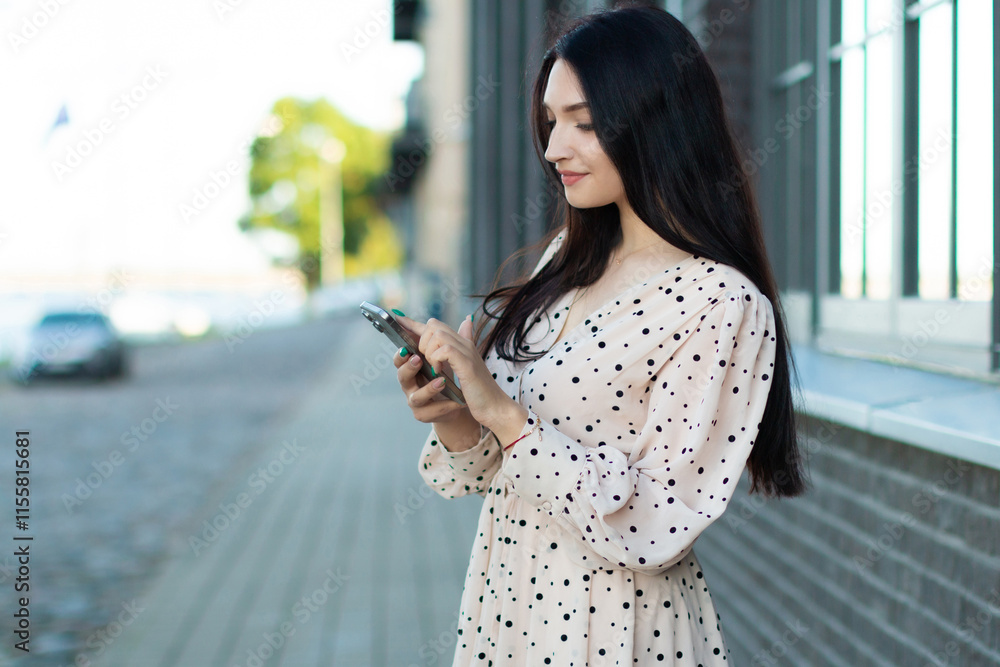 Fototapeta premium Stylish woman in polka dot dress using smartphone outdoors – modern communication, fashionable lifestyle and urban elegance in a city.
