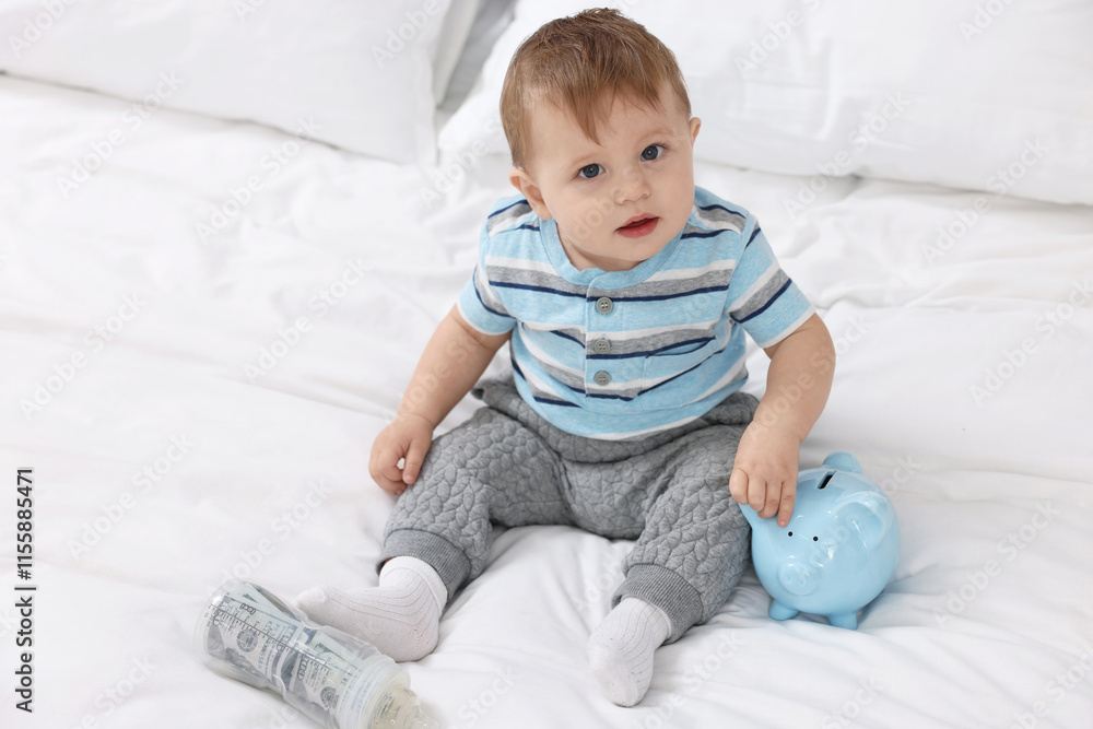 Cute little baby with money in bottle and piggybank on bed at home Cute little baby with money in bottle and piggybank on bed at home