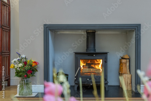 Cozy wood burner in a modern house. Minimalist real estate lifestyle photo of a fireplace with logs and flowers next to a wood burner