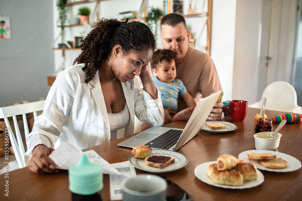 Stressed mother working on laptop while father entertains toddler during breakfast at home Stressed mother working on laptop while father entertains toddler during breakfast at home