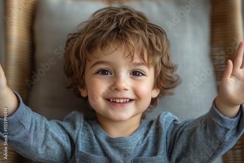 Young child with curly hair smiling and raising arms in a cozy setting indoors