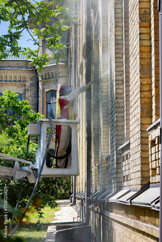 Obraz na płótnie Worker on an elevating platform cleaning the facade of an old brick building during sunny weather w salonie