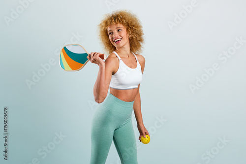 Young Latina girl with blonde afro hair smiling standing with a pickleball paddle