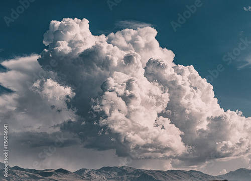 Dramatic cumulonimbus cloud forming above a mountain range, creating a stunning contrast between the bright white clouds and the dark blue sky photo