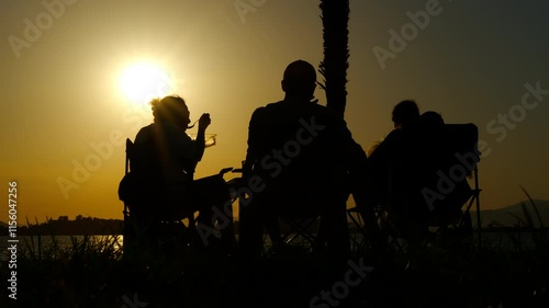 Family enjoying sunset conversation. Vibrant sunset casts silhouettes of a family sharing a peaceful moment by the lake, engaging in heartfelt conversation and enjoying the tranquility of the evening