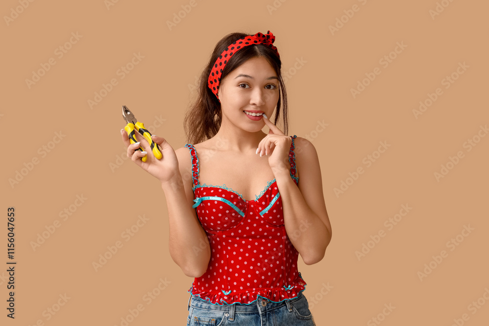 Beautiful young Asian pin-up woman with pliers on brown background Beautiful young Asian pin-up woman with pliers on brown background