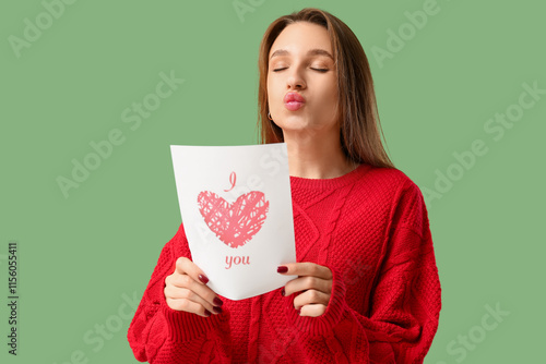 Beautiful young woman with greeting card on green background. Valentine's Day celebration