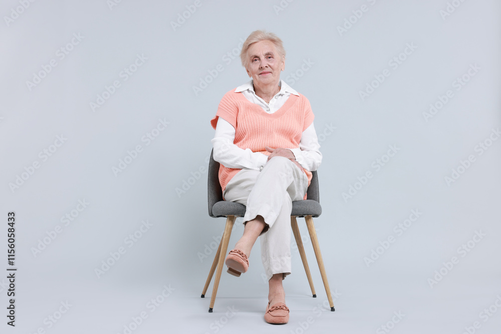 Fototapeta premium Senior woman on chair against light background