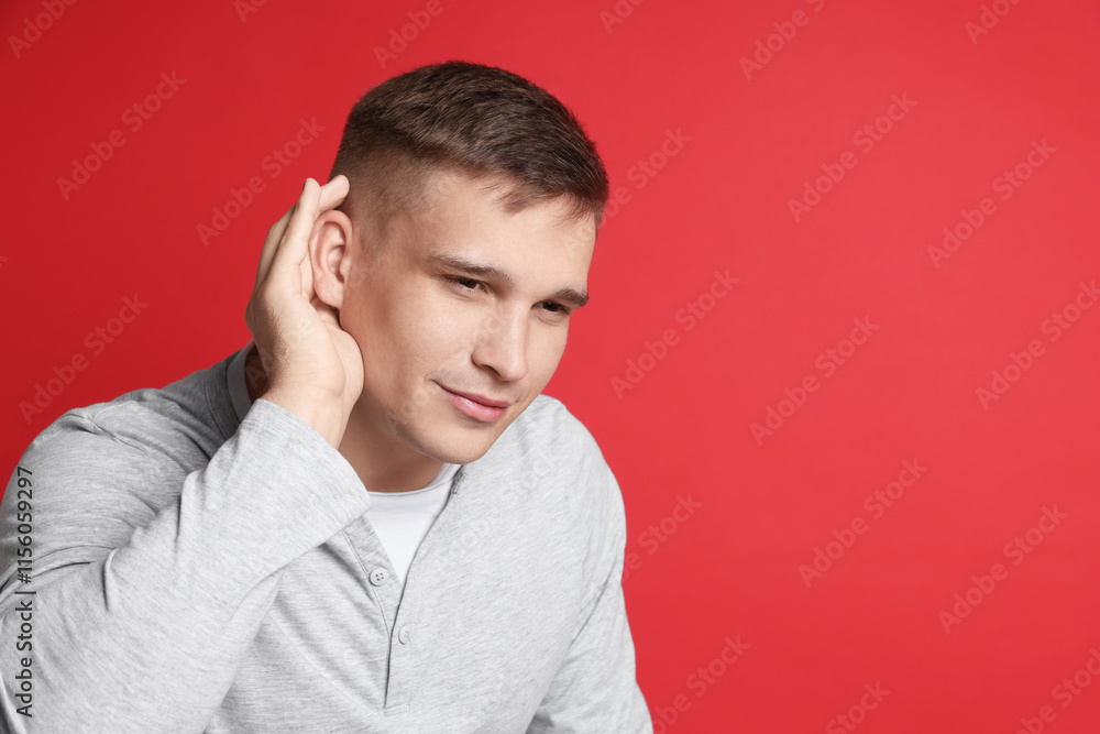Man showing hand to ear gesture on red background, space for text Man showing hand to ear gesture on red background, space for text