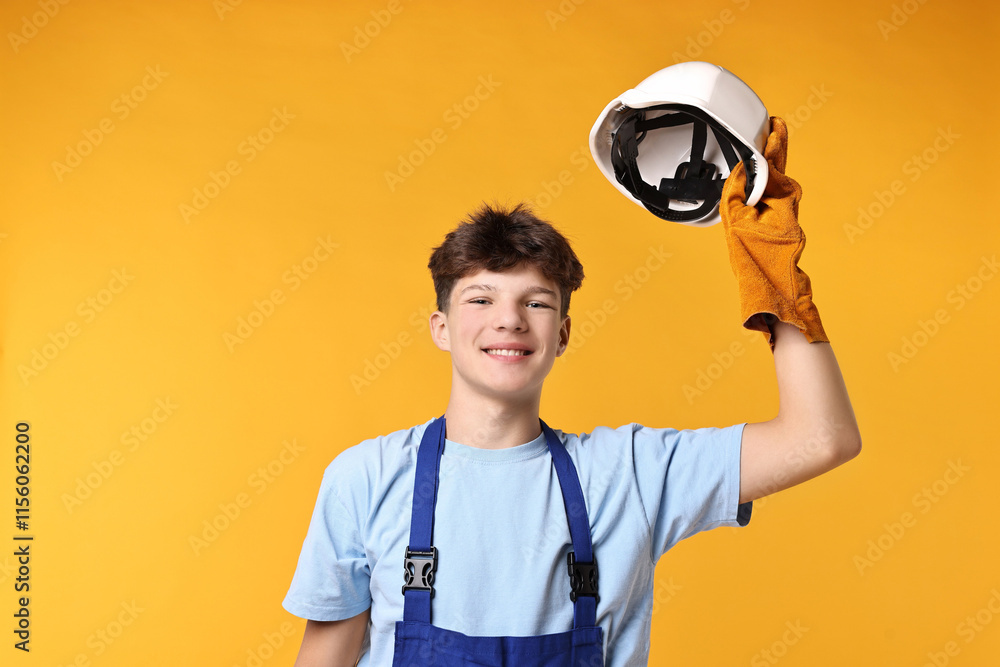 Teenage boy in hardhat working as builder on orange background Teenage boy in hardhat working as builder on orange background