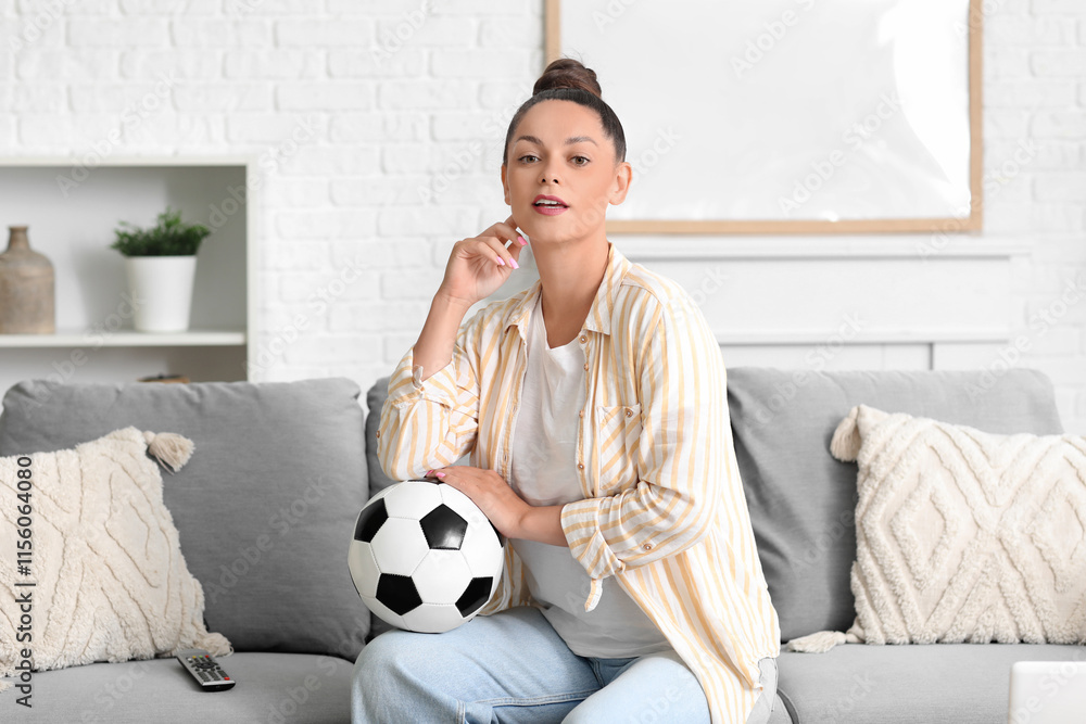 Beautiful young woman with soccer ball watching football on sofa at home Beautiful young woman with soccer ball watching football on sofa at home