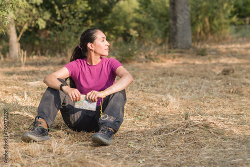 Hiker woman relaxing during orienteering race in forest looking at map with compass. Latin young venezuelan