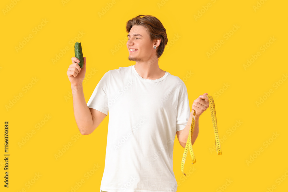 Sporty young man with cucumber and tape measure on yellow background. Weight loss concept Sporty young man with cucumber and tape measure on yellow background. Weight loss concept