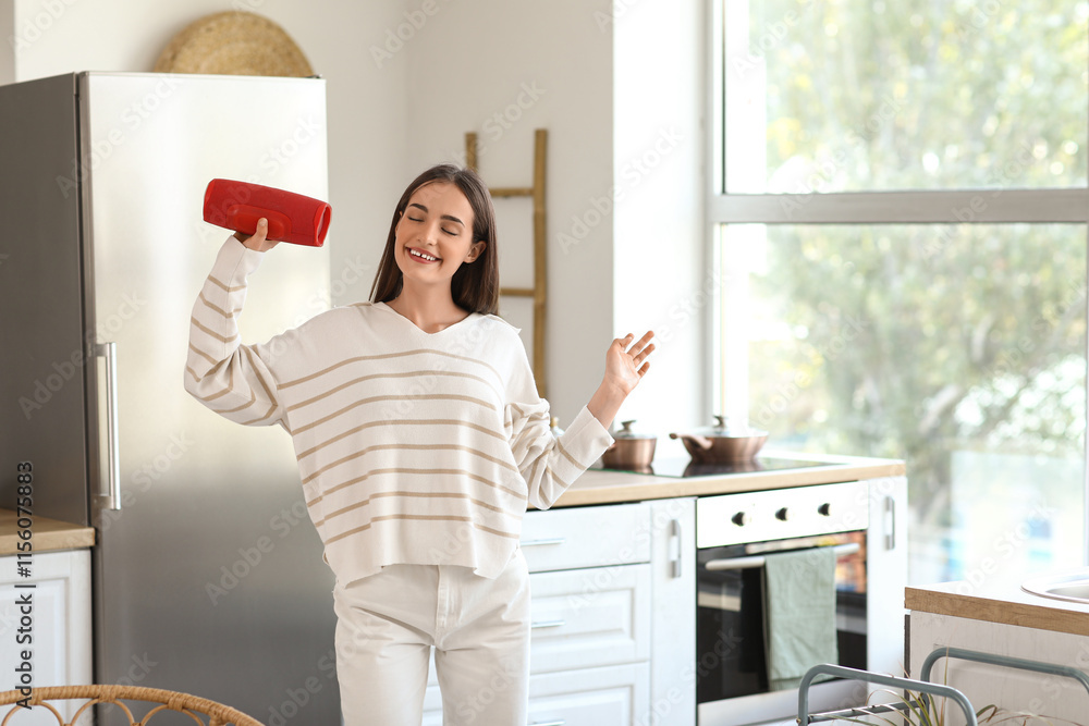 Beautiful young happy woman with wireless portable speaker in kitchen at home