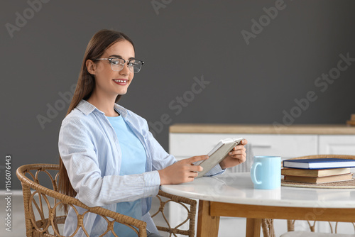 Smiling young woman in glasses reading book at white table, home learning and...