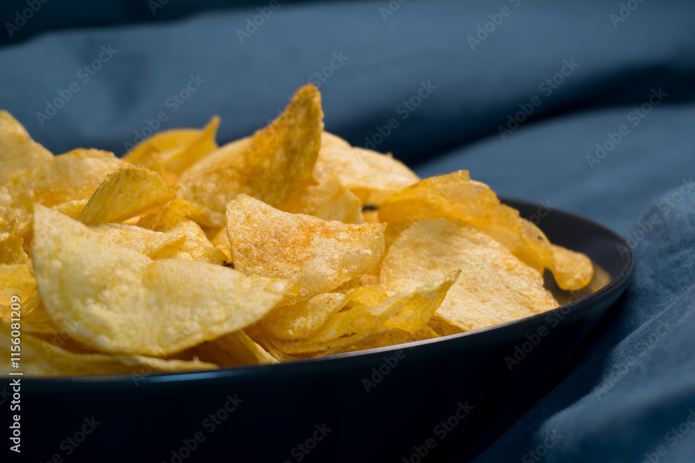 Golden potato chips in a black bowl: A tempting close-up of crispy golden potato chips served in a stylish black bowl against a deep blue background. Golden potato chips in a black bowl: A tempting close-up of crispy golden potato chips served in a stylish black bowl against a deep blue background.