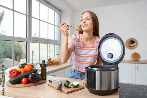 Young woman with multi cooker preparing food at table in kitchen photo