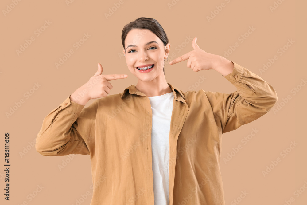 Smiling young woman pointing at dental braces on beige background Smiling young woman pointing at dental braces on beige background