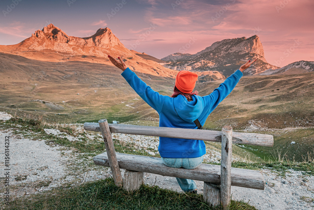 Φωτογραφία Female tourist sitting on wooden bench with arms raised, enjoying a breathtaking