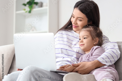 Young mother with her little daughter using laptop on sofa at home