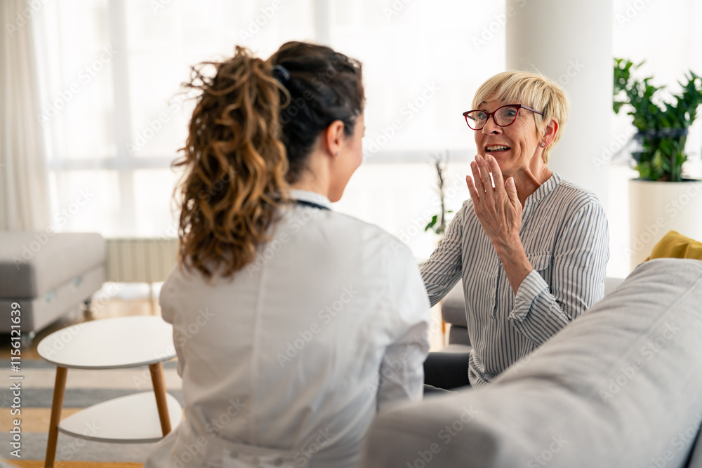 Obraz premium Caucasian female physician in white coat conducts friendly medical consultation with senior patient during residential healthcare visit, sharing positive interaction.