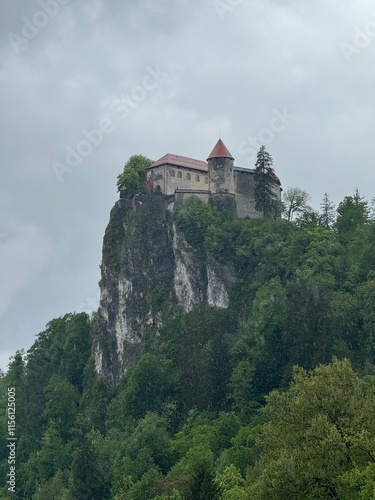 A majestic red-roofed castle perched atop a rugged rocky cliff in the picturesque town of Bled, Slovenia, set amidst lush greenery and surrounded by trees. photo