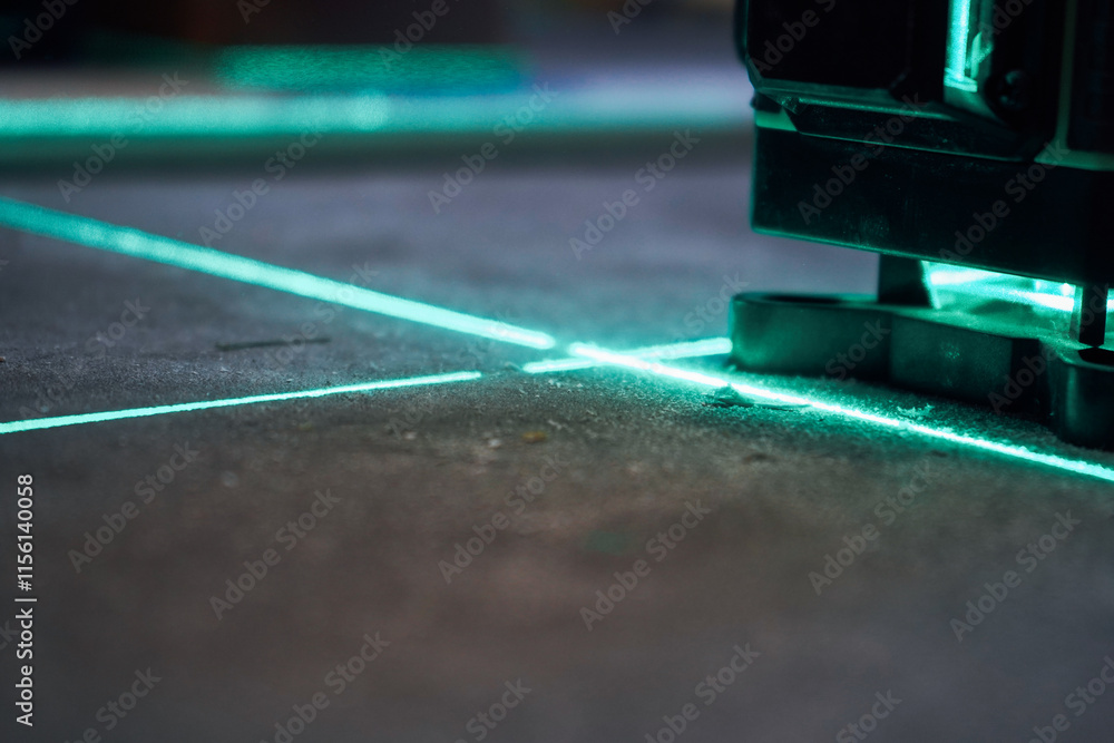 Laser level measuring tool with visible green laser beam on wall at construction site. Measuring level. Professional equipment for installing stretch ceiling. Home renovation concept, close up Laser level measuring tool with visible green laser beam on wall at construction site. Measuring level. Professional equipment for installing stretch ceiling. Home renovation concept, close up