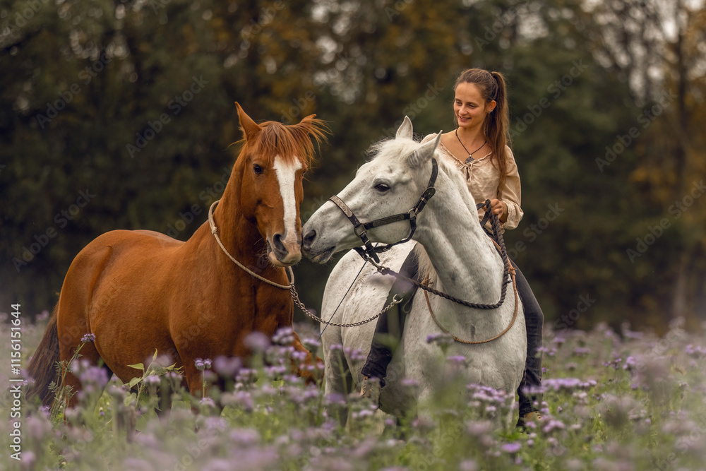 Horsemanship concept: A woman interacts with her two horses at a flower field in autumn outdoors Horsemanship concept: A woman interacts with her two horses at a flower field in autumn outdoors