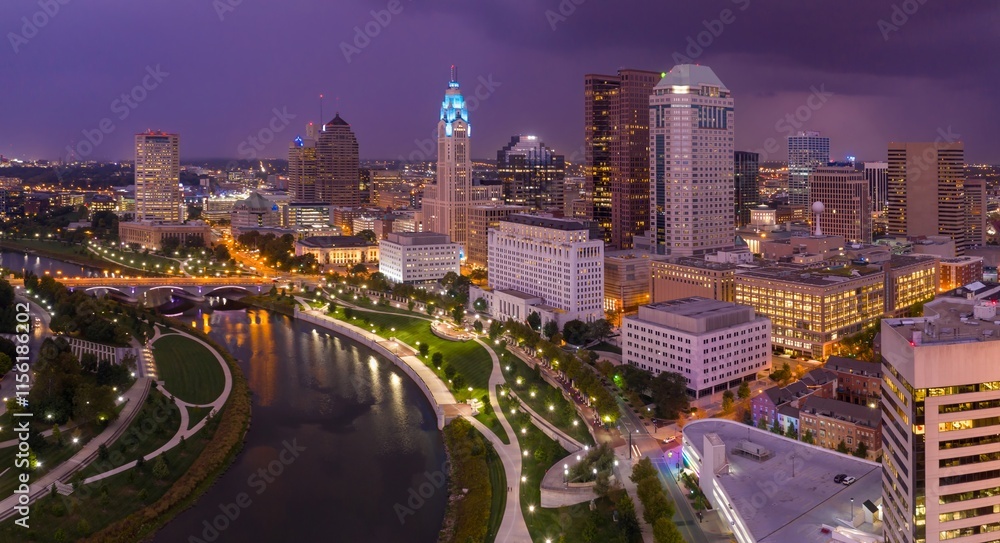 Fototapeta premium Evening cityscape of downtown Columbus, Ohio. Illuminated buildings and parkland along the Scioto River. Aerial view. DOWNTOWN, COLUMBUS, OHIO, UNITED STATES