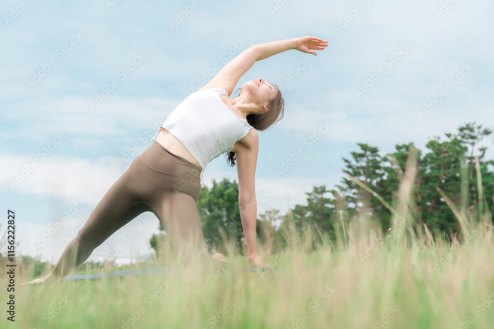 Fototapeta premium 草原の中でヨガ・ストレッチ・ピラティス・ボディケアをする女性(ヘルスケア・ダイエット・健康維持) 