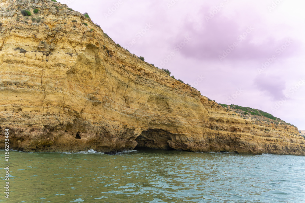 Stunning coastal cliffs with intricate sea caves, showcasing layers of golden and reddish rock formations. The turquoise waters add to the breathtaking scenery. Algarve, Portugal.