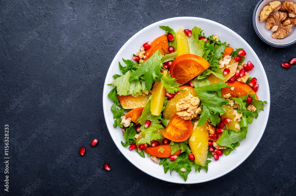 Winter vegan persimmon salad with pomegranate, walnuts, oranges and lettuce, black background, top view Winter vegan persimmon salad with pomegranate, walnuts, oranges and lettuce, black background, top view