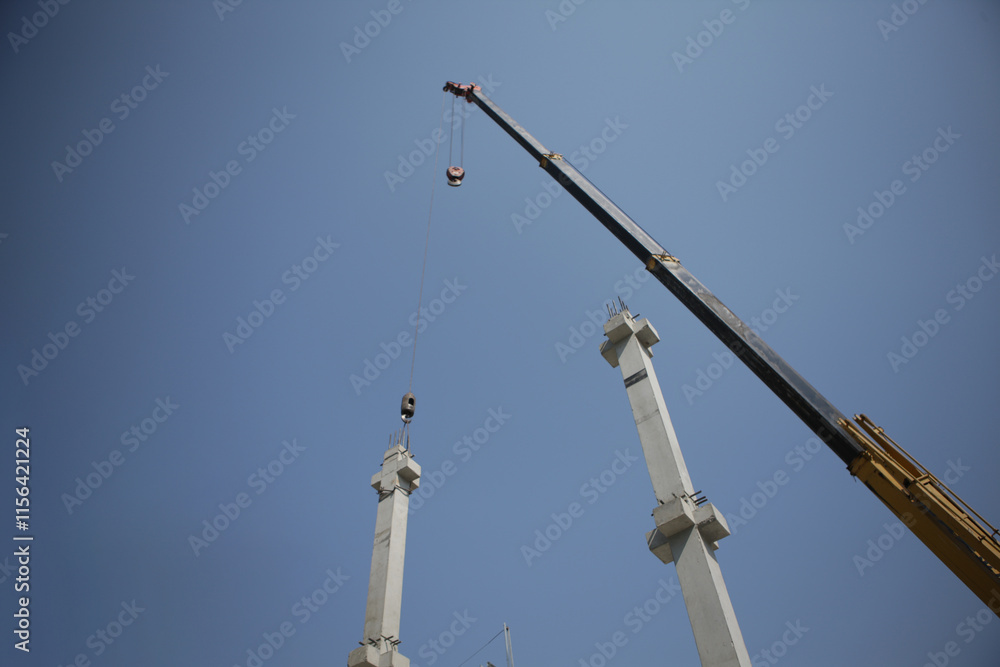 Crane Lifting Concrete Columns with Wire Rope Sling Against Clear Sky Crane Lifting Concrete Columns with Wire Rope Sling Against Clear Sky