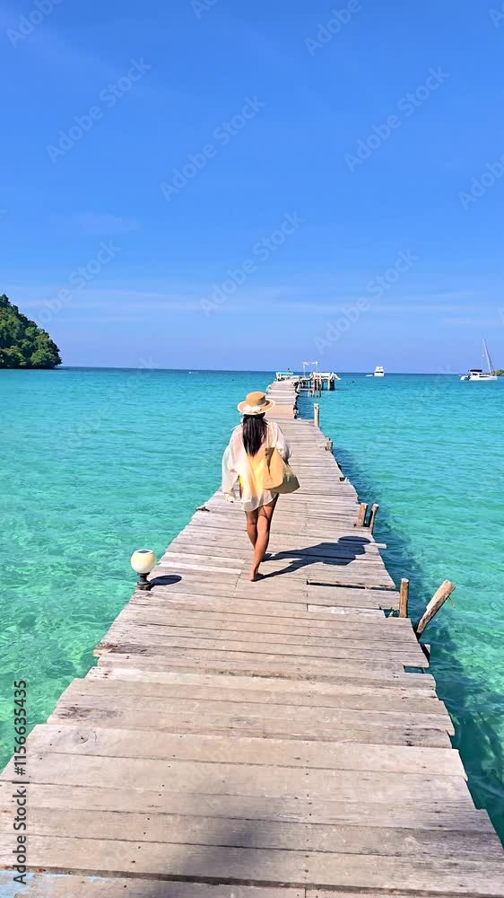 A vibrant journey unfolds as a traveler walks along a picturesque wooden pier, surrounded by the crystal-clear blue waters of Koh Kood, Thailand. The scenic landscape beckons exploration. A vibrant journey unfolds as a traveler walks along a picturesque wooden pier, surrounded by the crystal-clear blue waters of Koh Kood, Thailand. The scenic landscape beckons exploration.